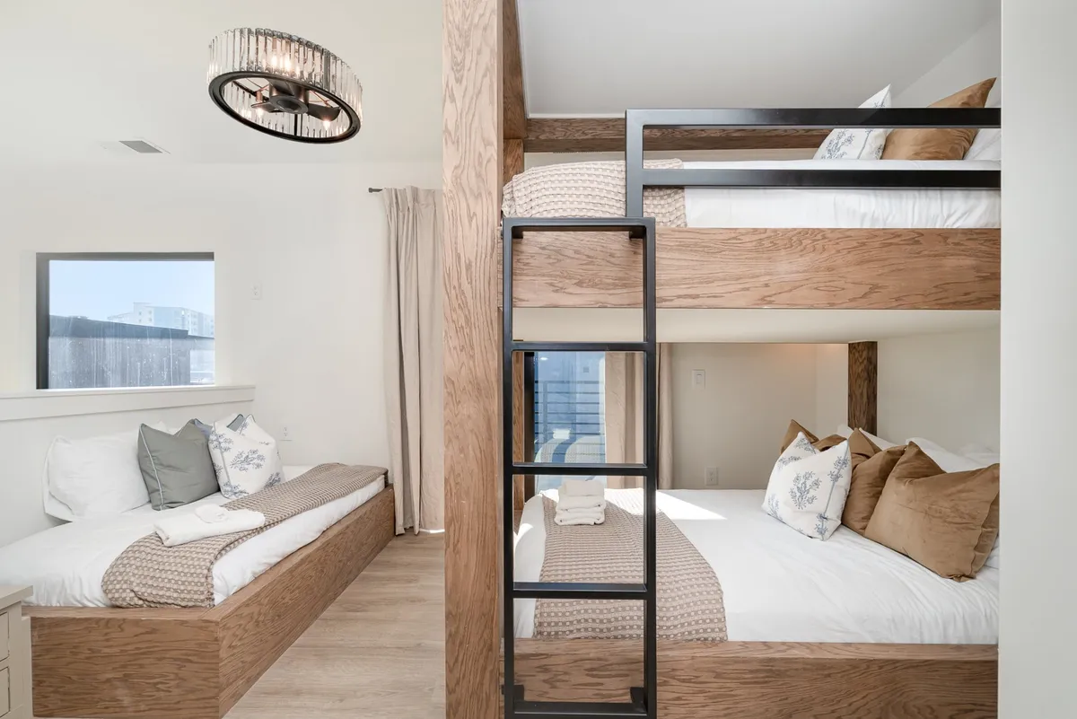 A comfortable bedroom with a queen-over-queen bunk bed, a separate twin daybed, playful decorative pillows, and soft lighting. The space feels fun and flexible, perfect for families or friends, and invites a sense of togetherness and adaptability.