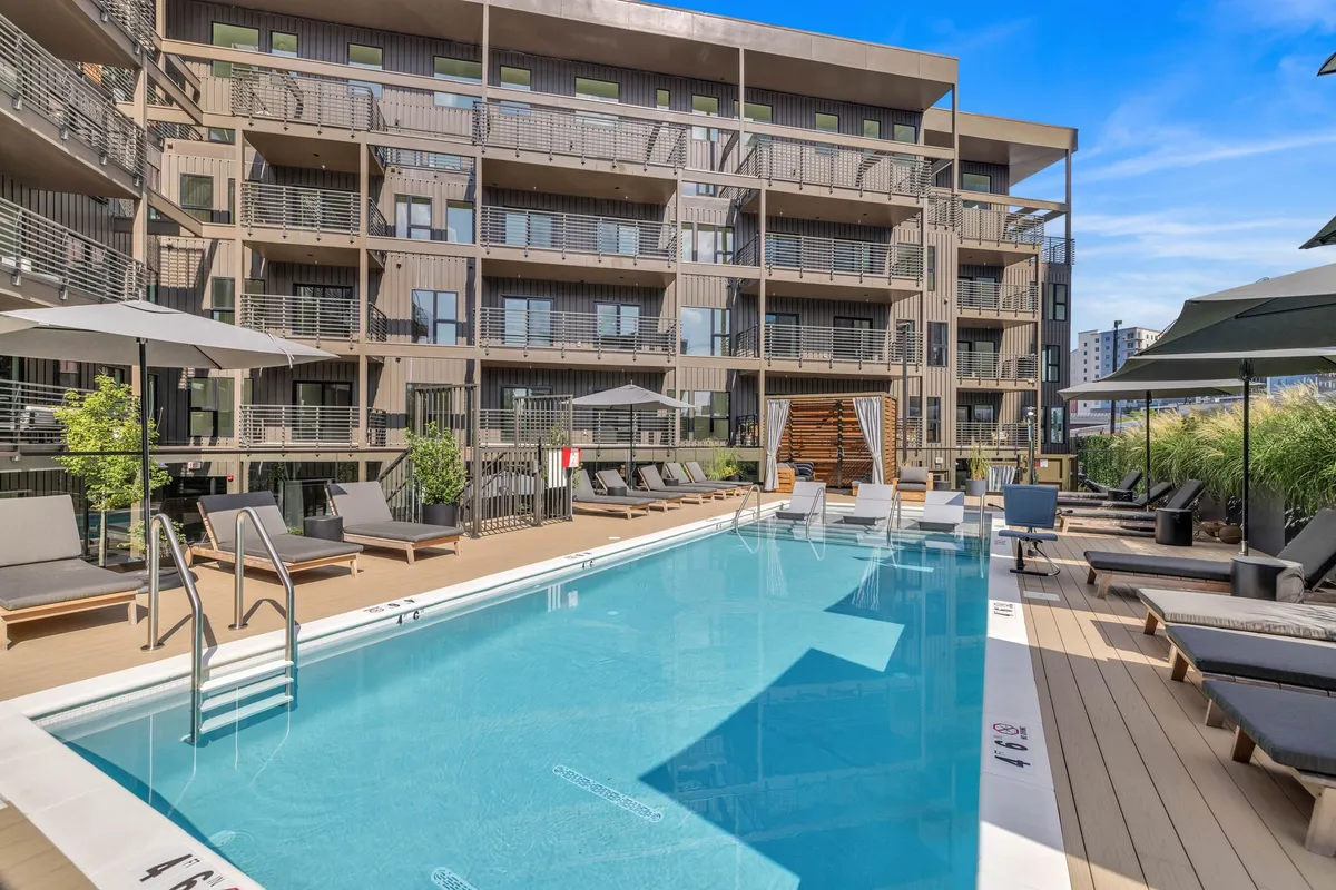 A serene swimming pool surrounded by lounge chairs, green plants, and the building’s modern façade. The pool area invites guests to relax, socialize, and unwind after a day exploring Nashville’s attractions.