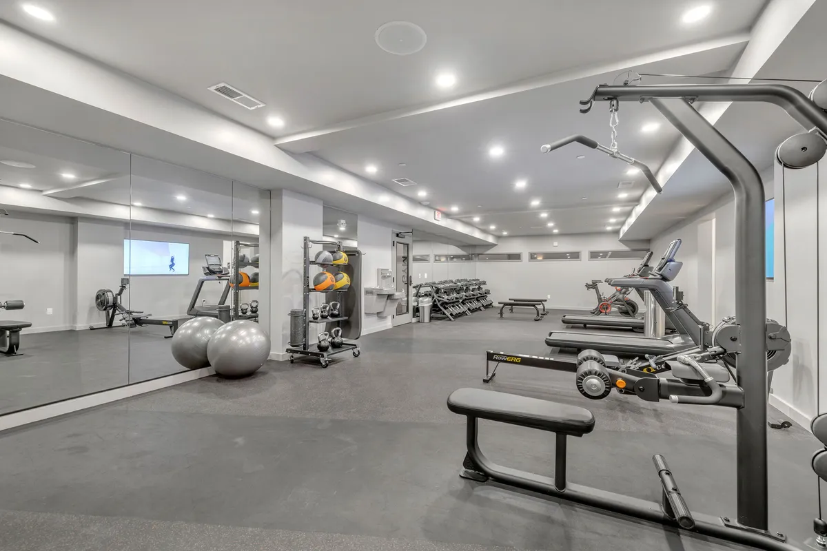 A spacious, modern fitness center equipped with various gym machines, large mirrors, and exercise balls. The area is well-lit and designed to inspire motivation and community workouts.
