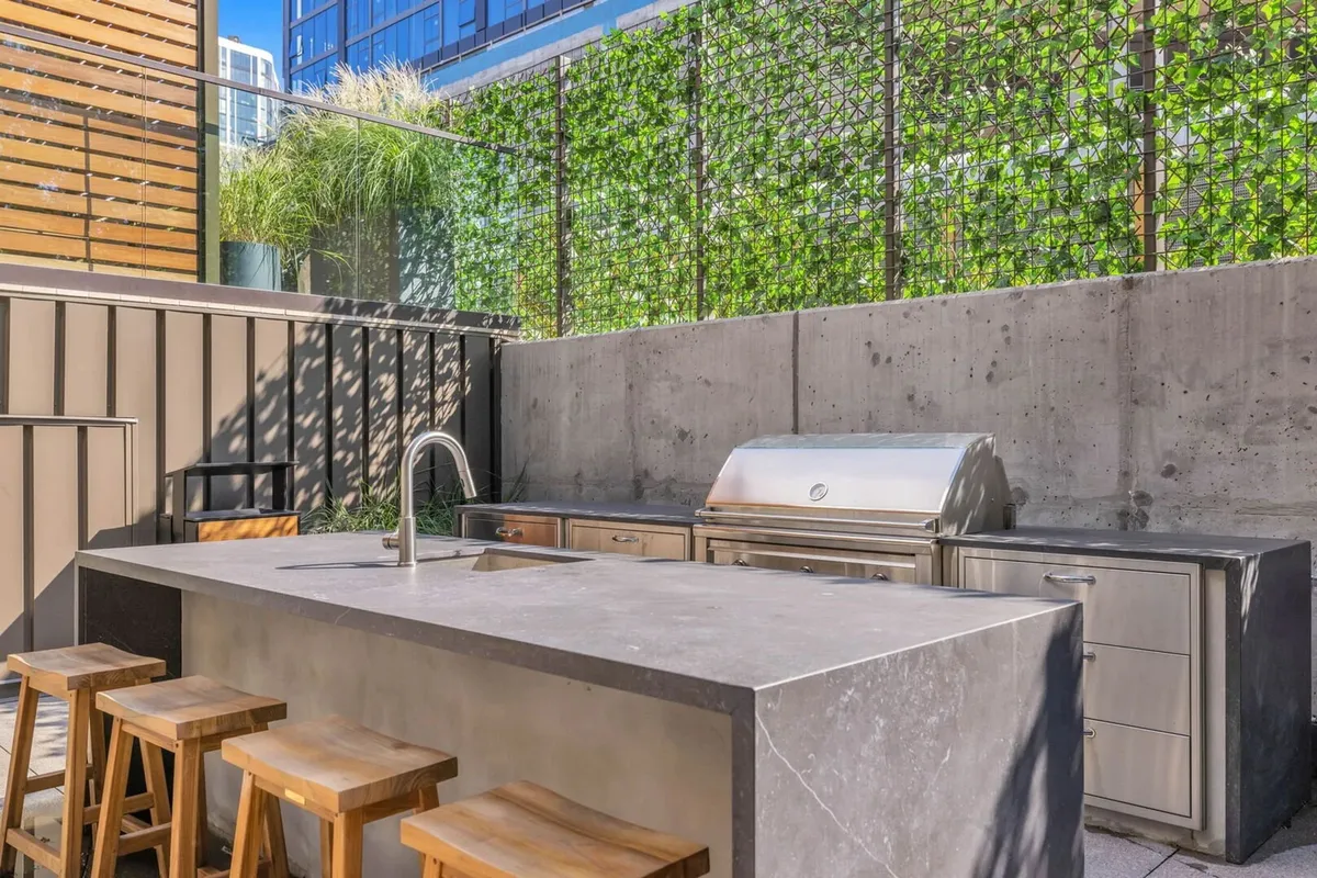 A sleek outdoor kitchen with a built-in grill, bar stools, and a lush green wall, perfect for barbecuing and entertaining guests in a modern open-air setting.