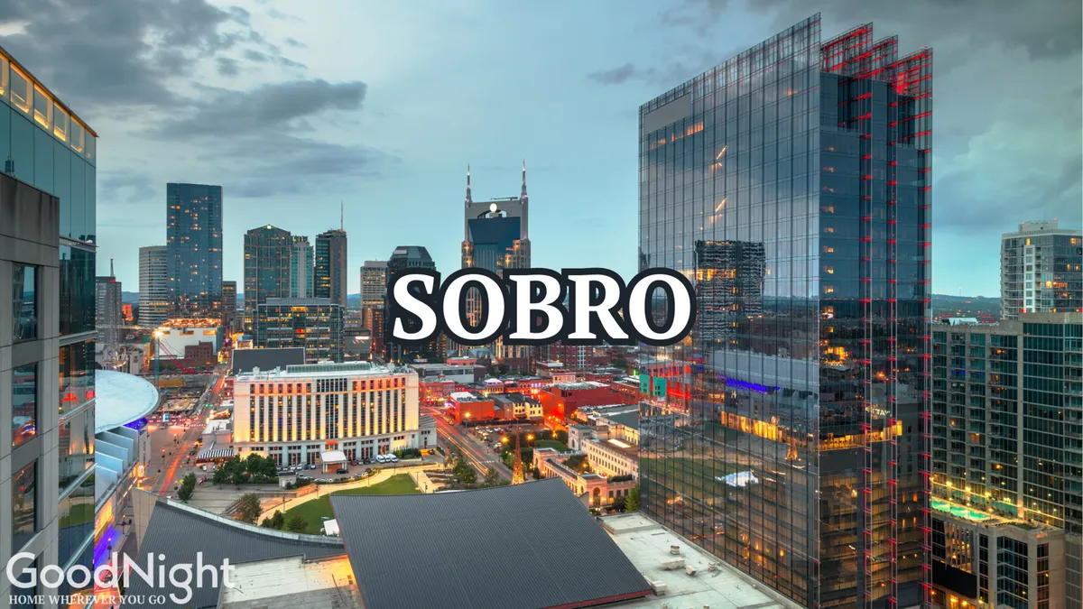 A striking skyline view of Nashville, illuminated at dusk, with 'SOBRO' prominently displayed. The energetic lighting and city activity capture the neighborhood's lively atmosphere and appeal to those seeking nightlife, dining, and spontaneous city exploration.