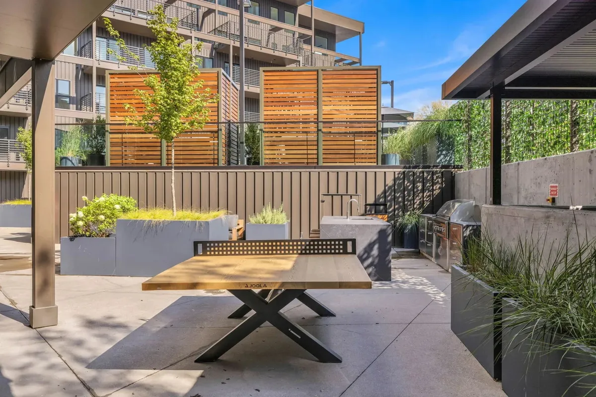 A lively outdoor barbecue area featuring a wooden table, decorative planters, and wooden screens. The space is ideal for casual gatherings, sunny brunches, and memorable BBQ parties with friends and family.