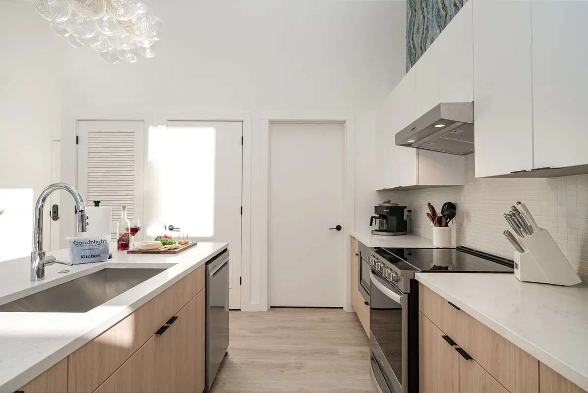 This image features a contemporary kitchen with a prominent kitchen island, stainless steel appliances, and a stylish chandelier. The space is designed for both cooking and entertaining, offering ample room for meal preparation and social gatherings.